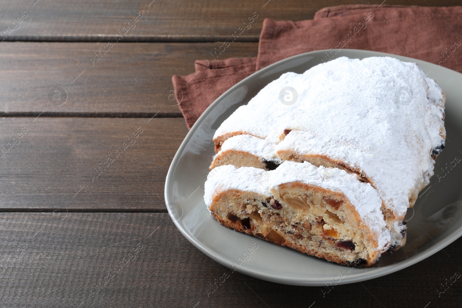 Photo of Traditional Christmas Stollen with icing sugar on wooden table, space for text