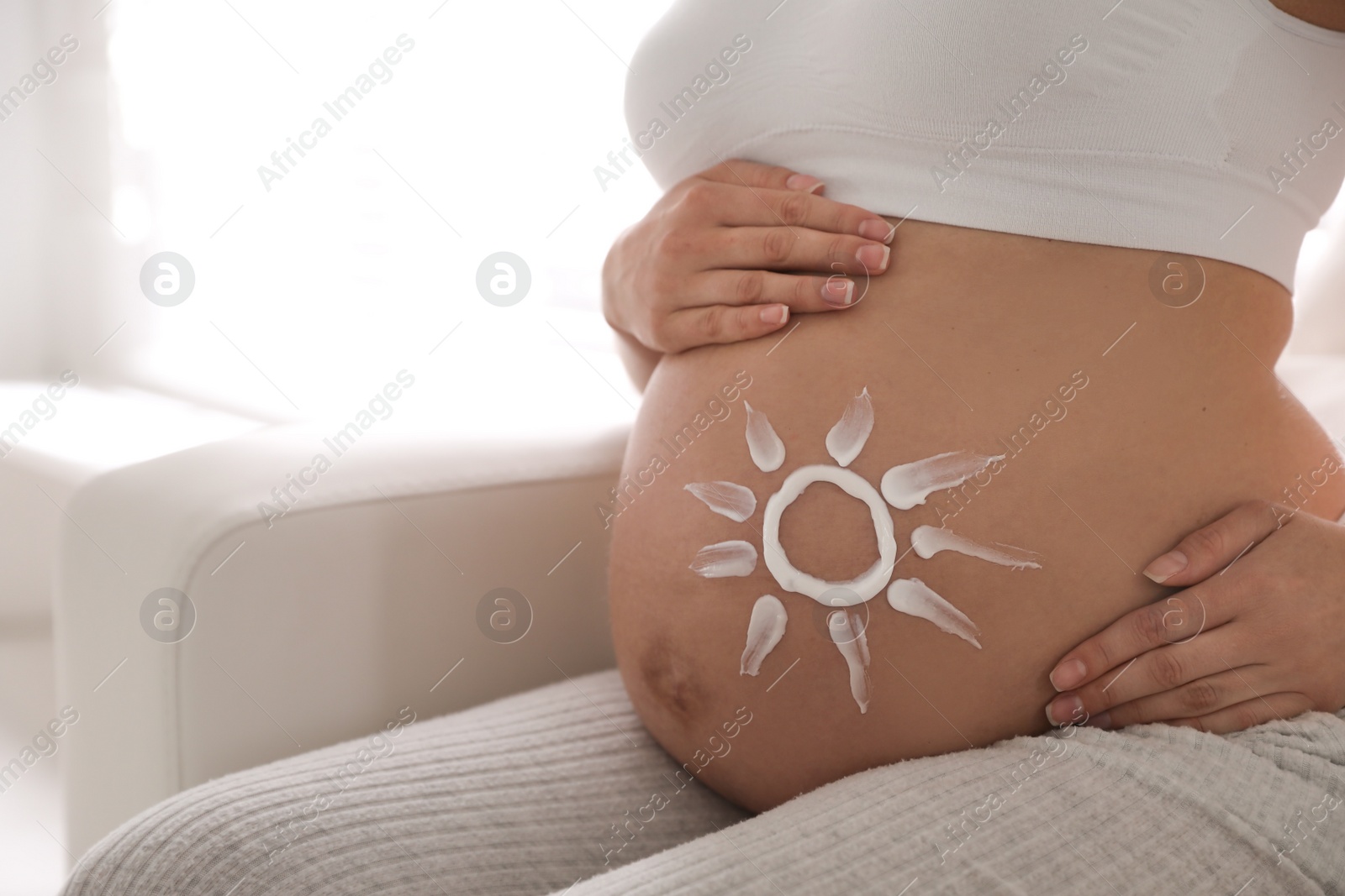 Photo of Young pregnant woman with sun protection cream on belly indoors, closeup. Space for text