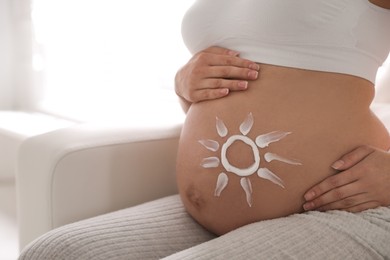 Young pregnant woman with sun protection cream on belly indoors, closeup. Space for text