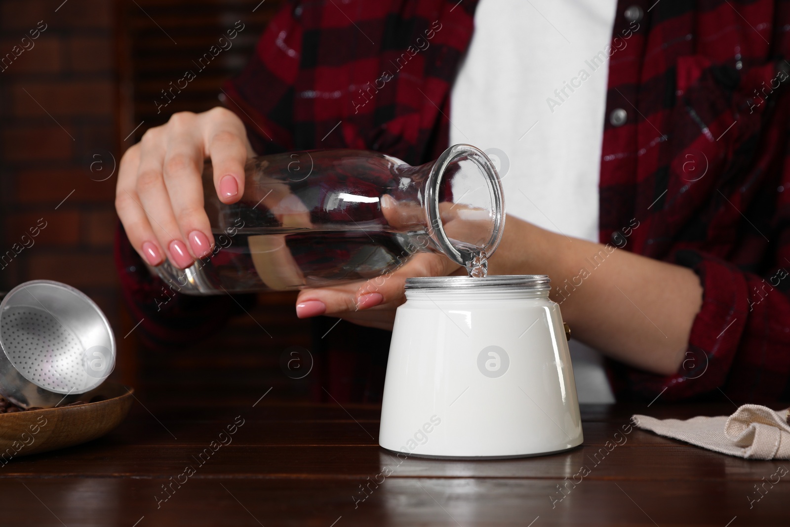 Photo of Brewing coffee. Woman pouring water into moka pot at wooden table indoors, closeup