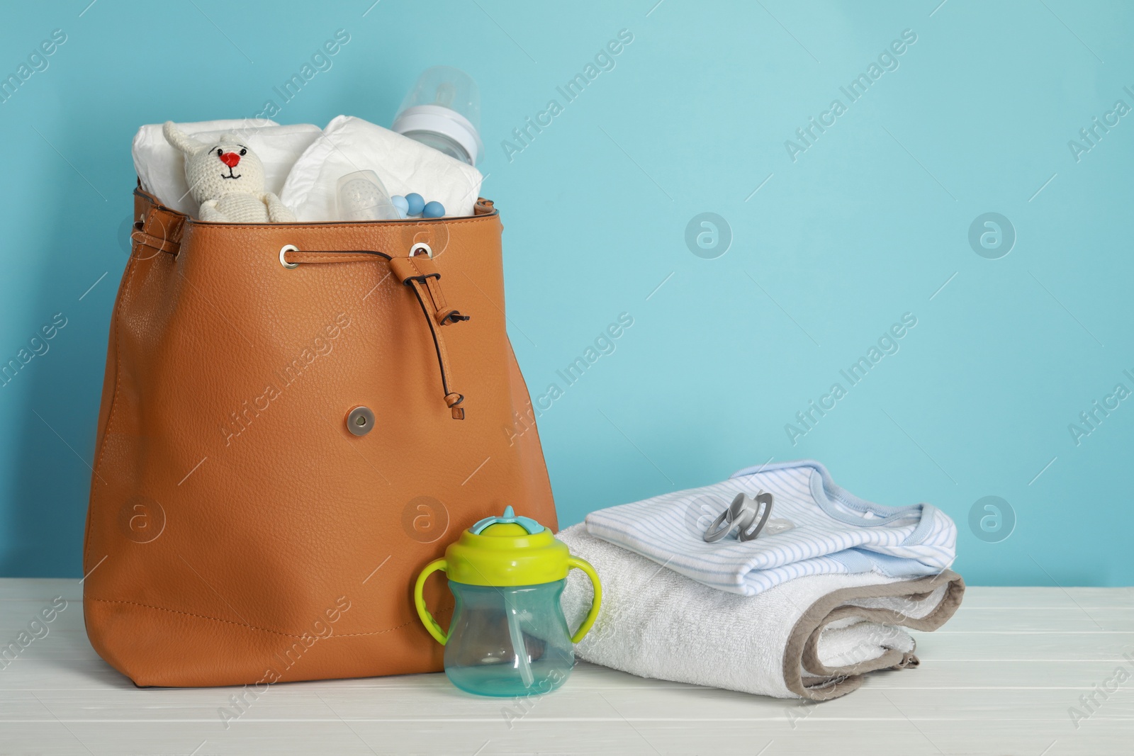 Photo of Mother's bag with baby's stuff on white wooden table against light blue background