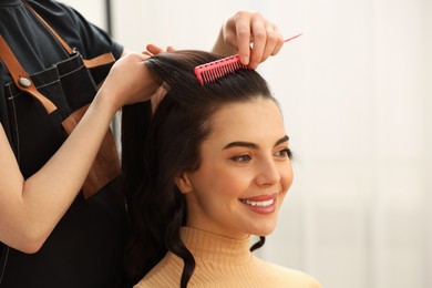 Professional hairdresser combing woman's hair indoors, closeup. Space for text