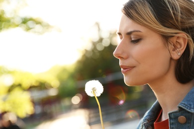 Young woman with dandelion in park on sunny day. Allergy free concept