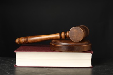 Photo of Wooden gavel, sound block and book on dark textured table, closeup