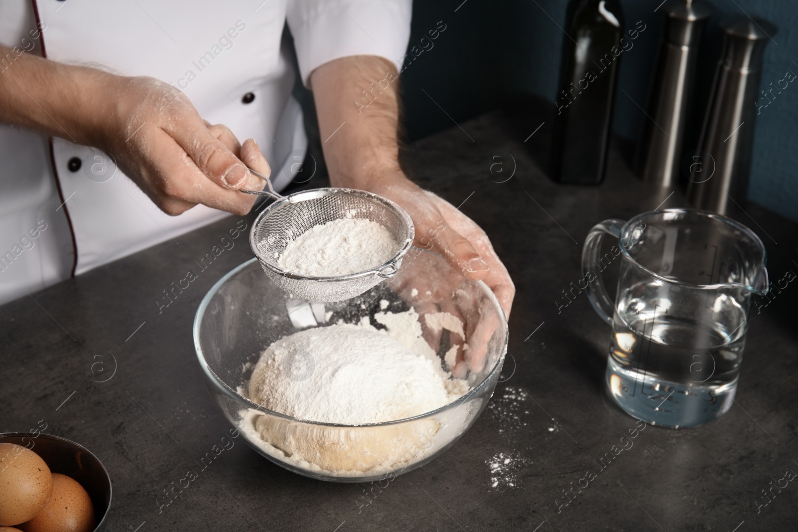 Photo of Man sprinkling dough for pastry with flour on table