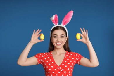 Photo of Beautiful woman in bunny ears headband holding Easter eggs on color background