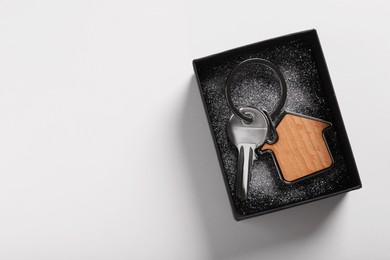 Key with trinket in shape of house and gift box on light grey background, top view with space for text. Housewarming party