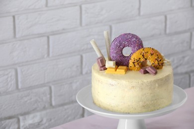 Delicious cake decorated with sweets on table near white brick wall, space for text