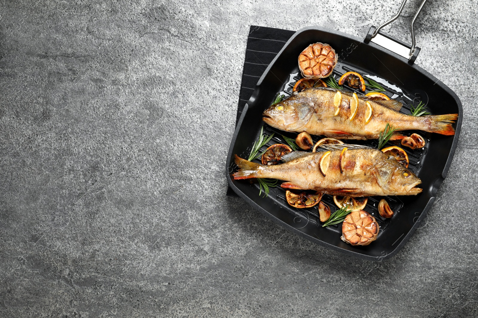 Photo of Tasty homemade roasted perches in grill pan on grey table, top view and space for text. River fish