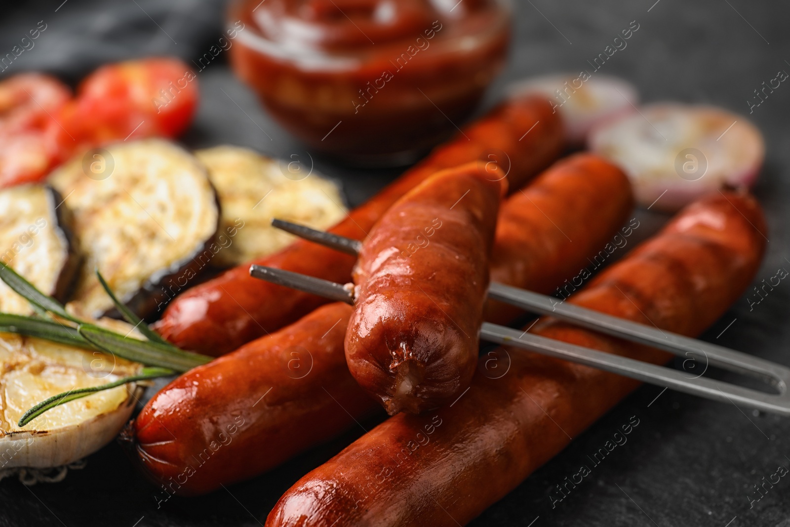 Photo of Delicious grilled sausages and vegetables on black table, closeup. Barbecue food