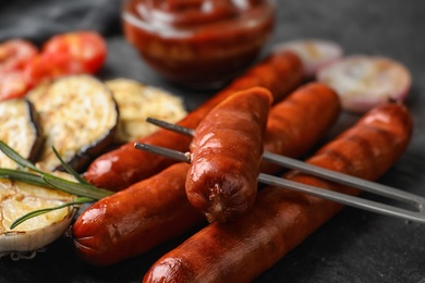 Delicious grilled sausages and vegetables on black table, closeup. Barbecue food