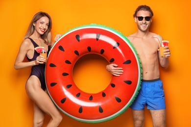 Photo of Happy young couple in beachwear with inflatable ring and cocktails on color background