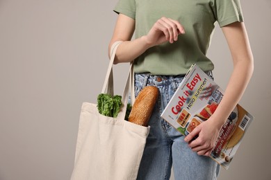 Woman with eco bag full of products and magazine on light background, closeup