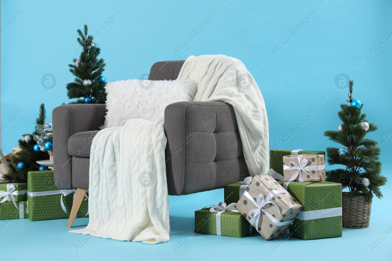 Photo of Beautiful Christmas themed photo zone with stylish armchair, trees and gift boxes on light blue background