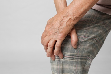 Senior woman having knee problems on grey background, closeup. Space for text