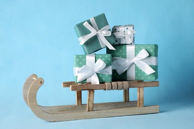 Photo of Wooden sleigh with Christmas gift boxes on light blue background