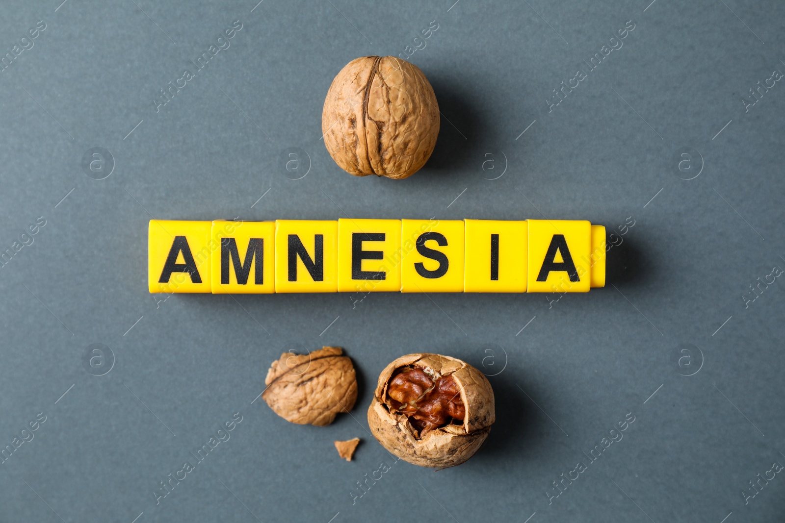 Photo of Word Amnesia made of yellow cubes and walnuts on grey background, flat lay