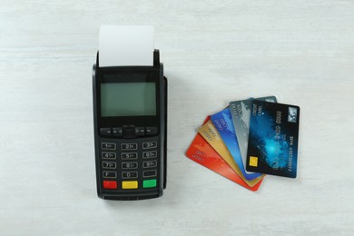 New modern payment terminal and credit cards on white wooden table, flat lay