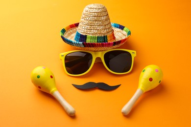 Photo of Mexican sombrero hat, sunglasses, fake mustache and maracas on orange background