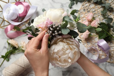 Photo of Florist creating beautiful bouquet at white marble table, top view