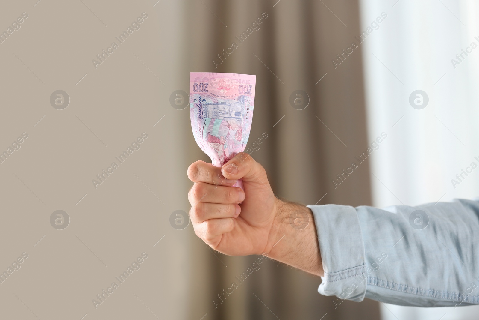 Photo of Man holding 200 Ukrainian Hryvnias banknote against blurred background, closeup with space for text. International relationships