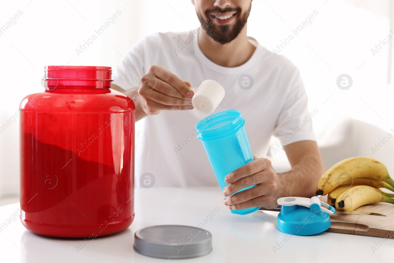 Photo of Young man preparing protein shake at table indoors, closeup