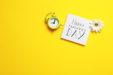 Photo of Flat lay composition of card with inscription HAPPY TEACHER'S DAY, flower and alarm clock on yellow background, space for text