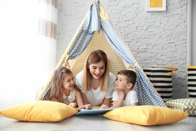 Photo of Nanny and little children reading book in tent at home