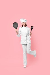 Professional chef with frying pan and spatula having fun on pink background