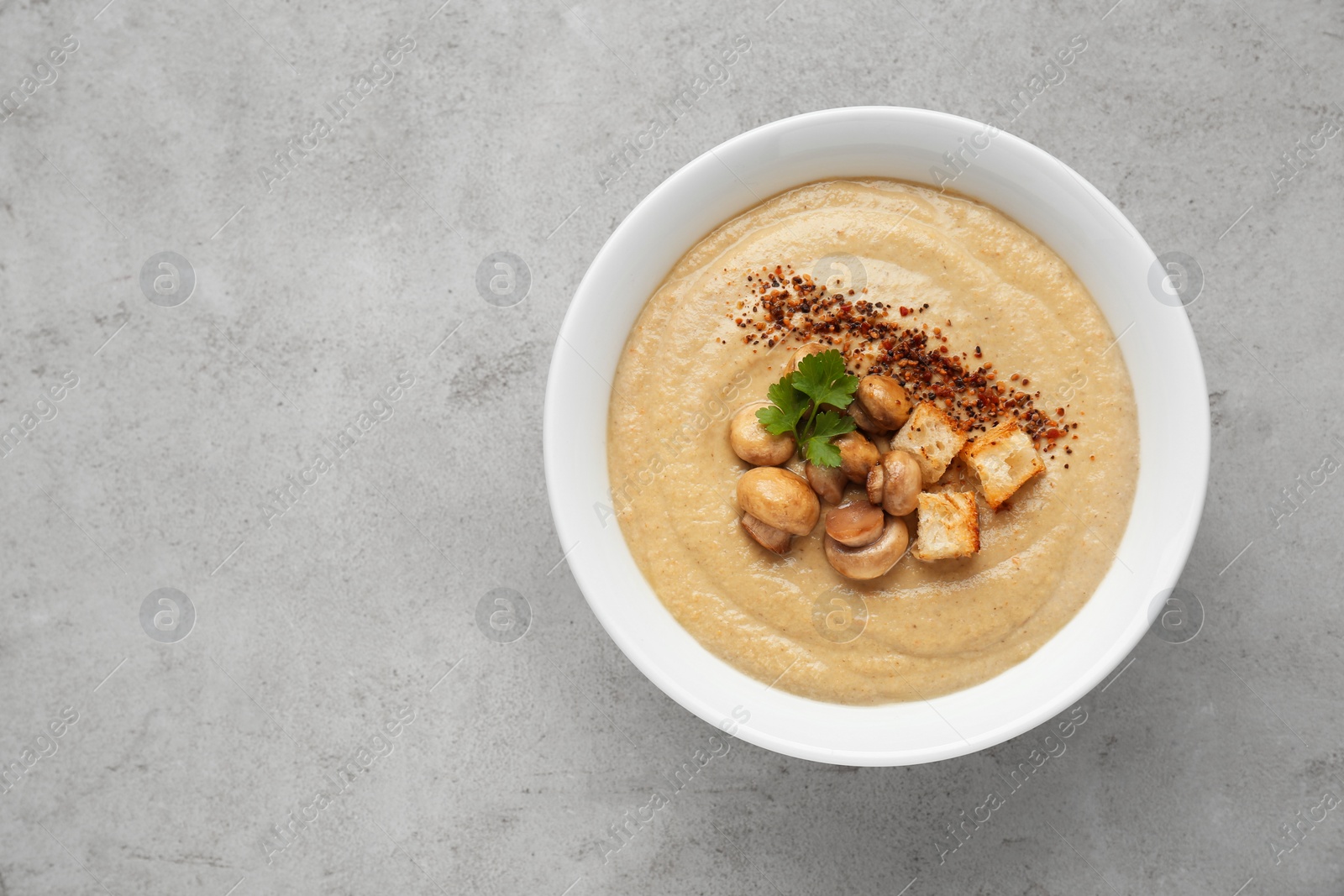 Photo of Delicious cream soup with mushrooms and croutons on beige textured table, top view. Space for text