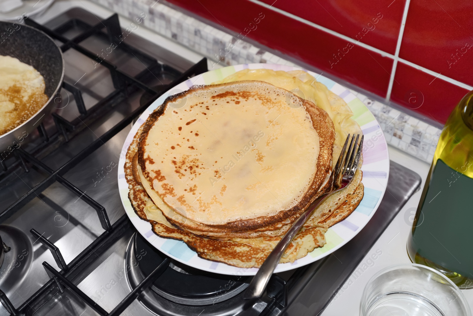 Photo of Plate of freshly made crepes with fork on stove in kitchen