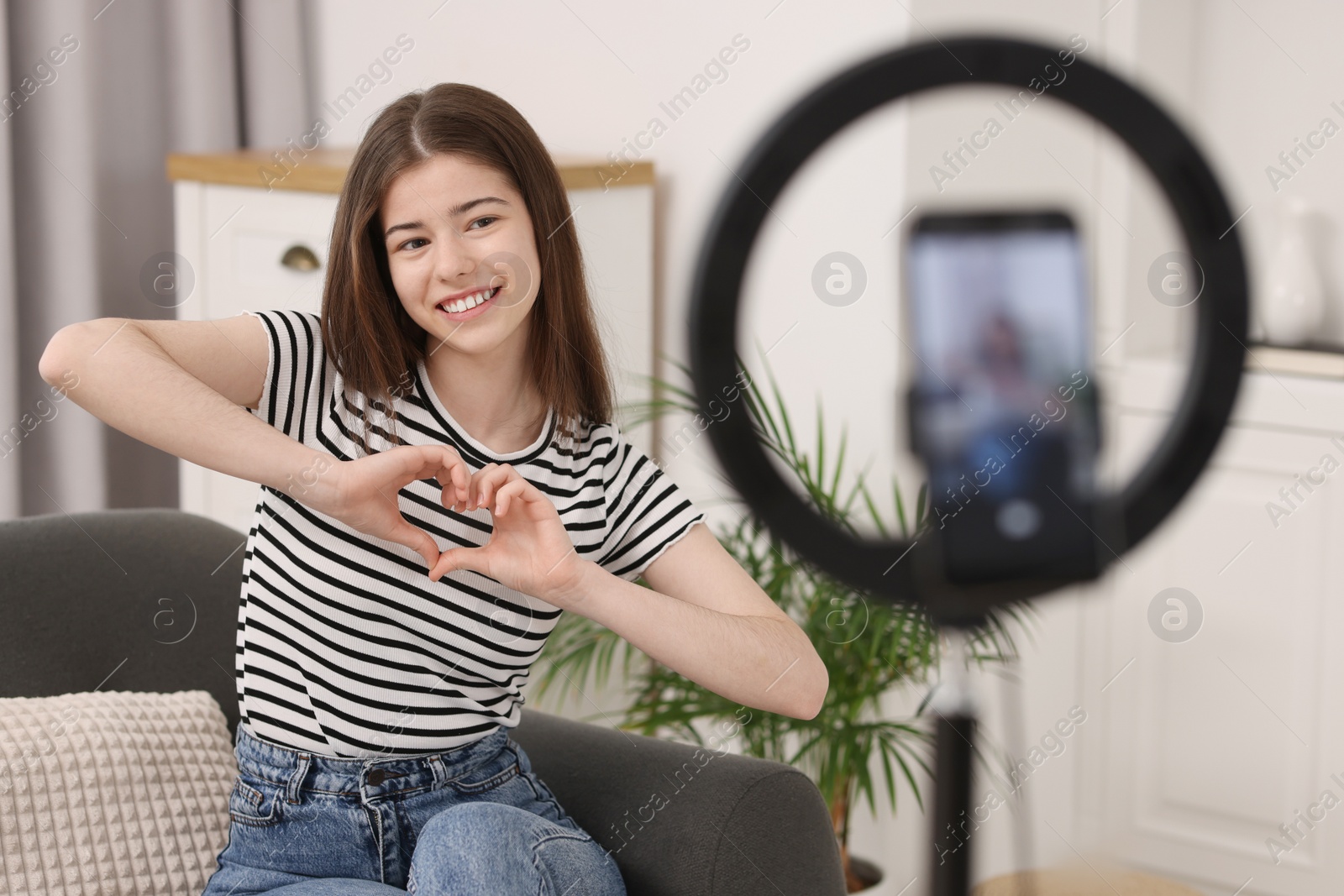 Photo of Smiling teenage blogger making heart gesture to her subscribers while streaming at home