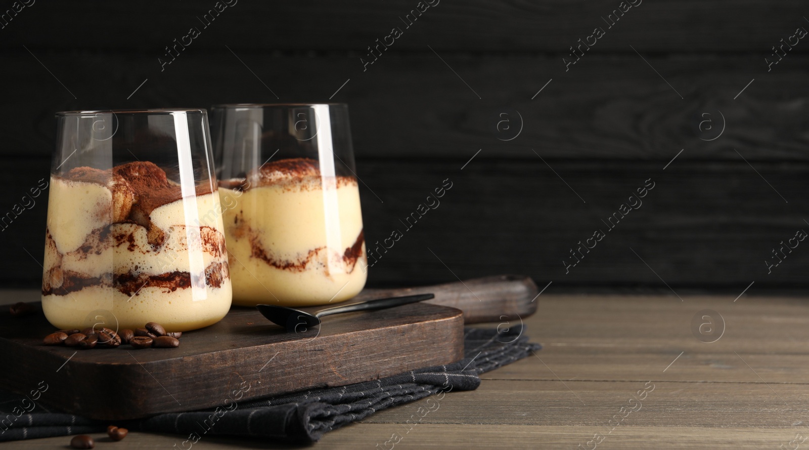 Photo of Delicious tiramisu in glasses, spoon and coffee beans on wooden table. Space for text