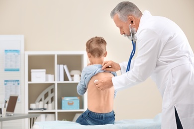 Photo of Doctor examining coughing little boy at clinic