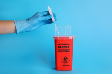 Photo of Doctor throwing used syringe into sharps container on light blue background, closeup