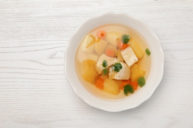 Homemade chicken soup in dish on wooden background, top view with space for text