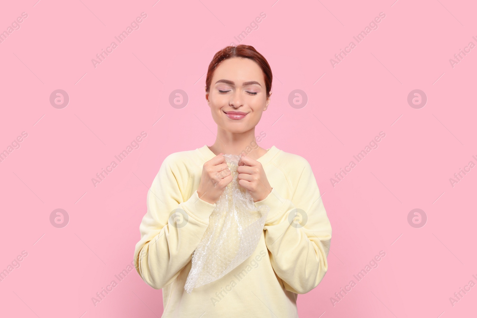 Photo of Woman popping bubble wrap on pink background. Stress relief