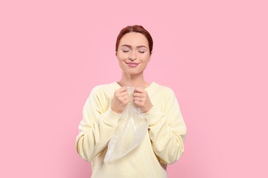 Photo of Woman popping bubble wrap on pink background. Stress relief