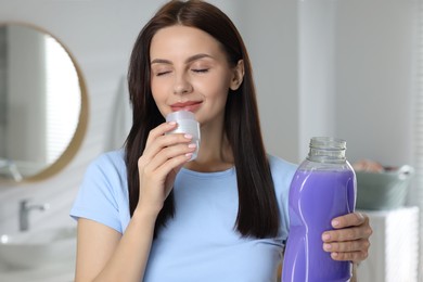 Photo of Beautiful woman smelling fabric softener in bathroom