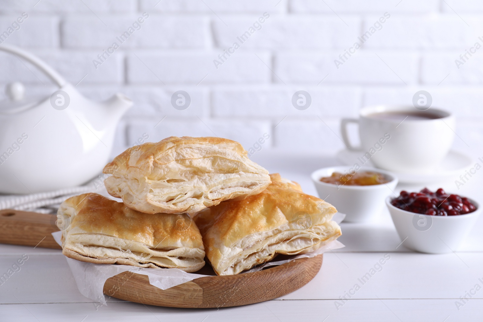 Photo of Delicious puff pastry served on white wooden table against brick wall