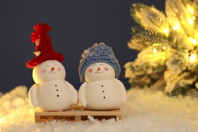Cute decorative snowmen and Christmas tree on artificial snow against dark background