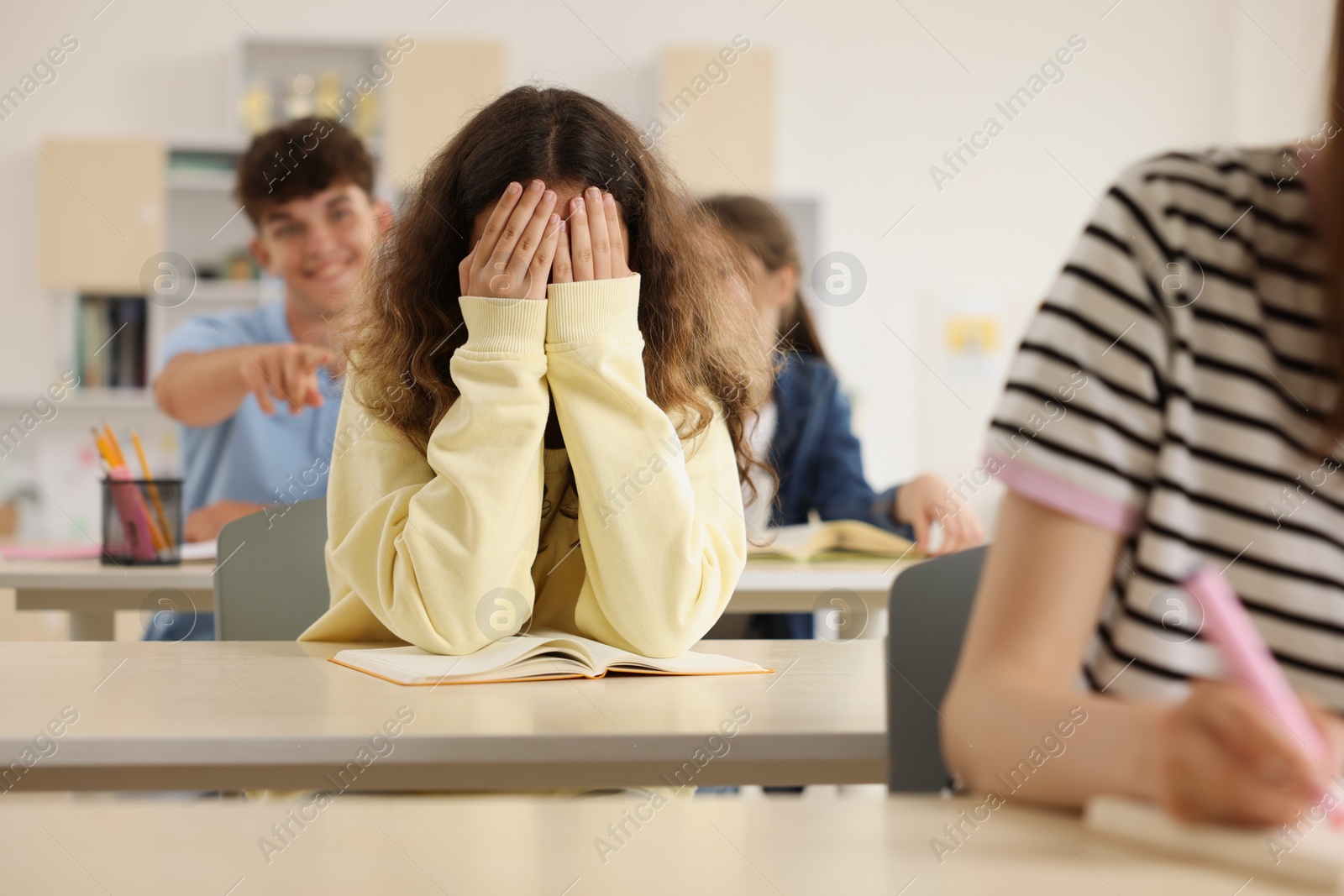 Photo of Teen problems. Lonely girl sitting separately from other students in classroom