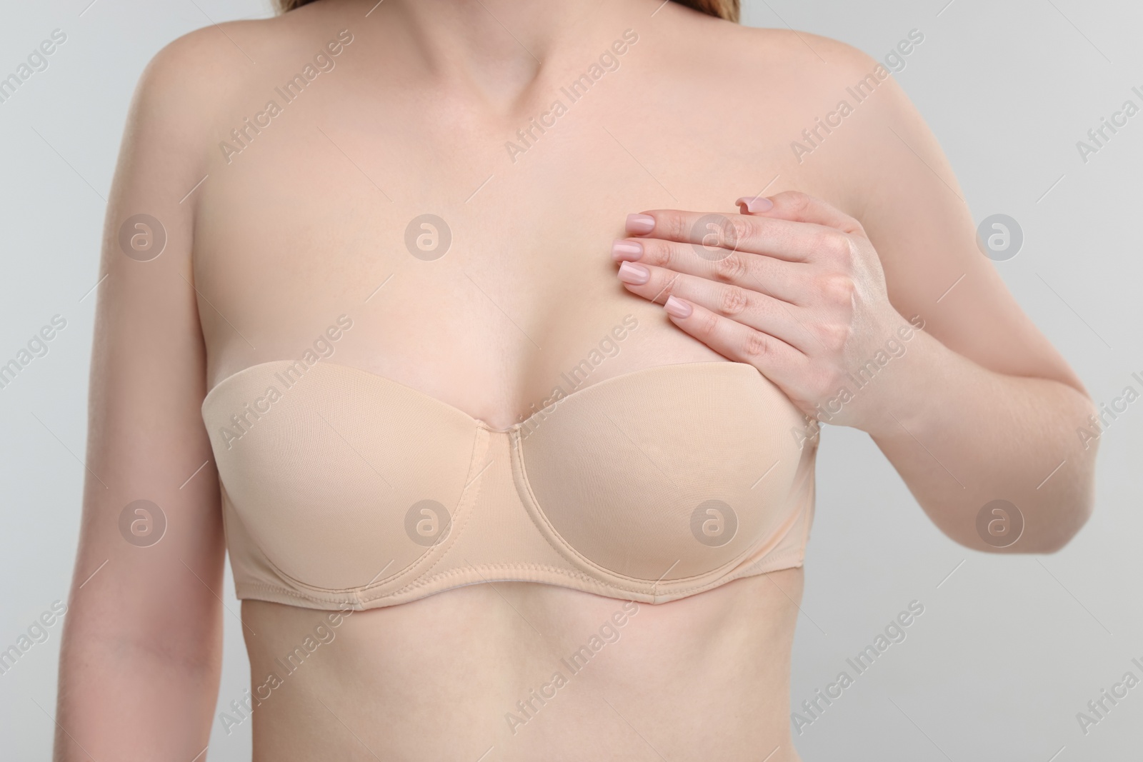 Photo of Mammology. Young woman doing breast self-examination on light grey background, closeup