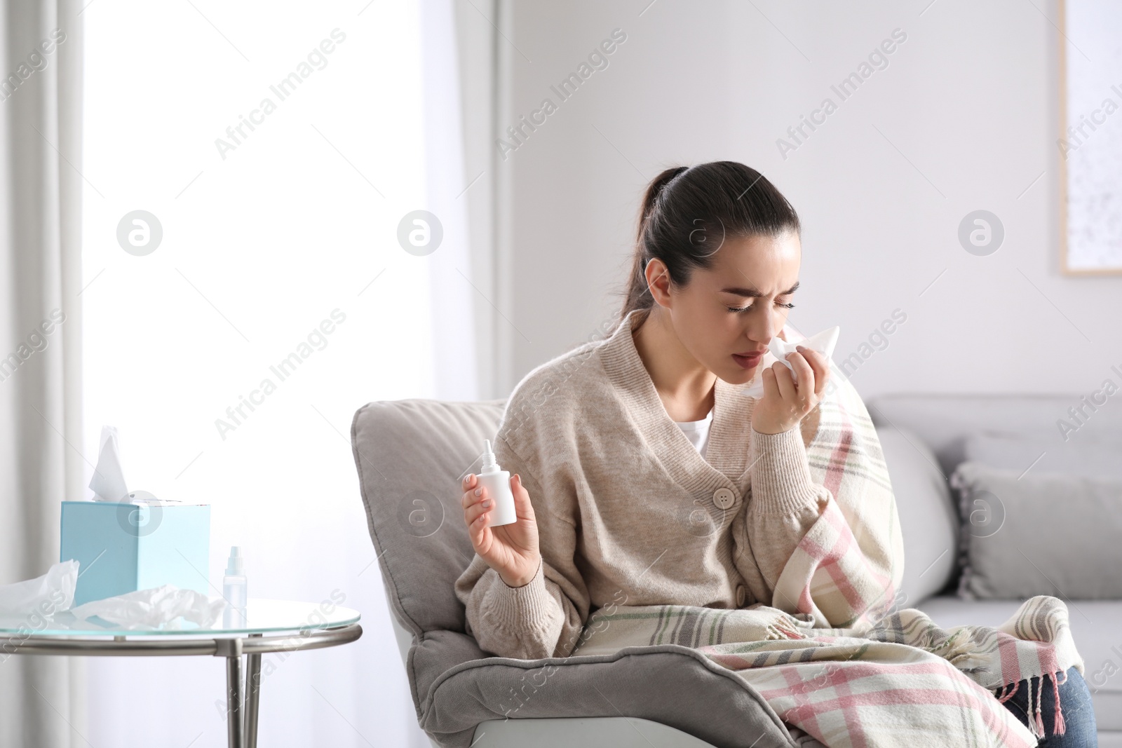 Photo of Sick young woman with napkins and nasal spray at home