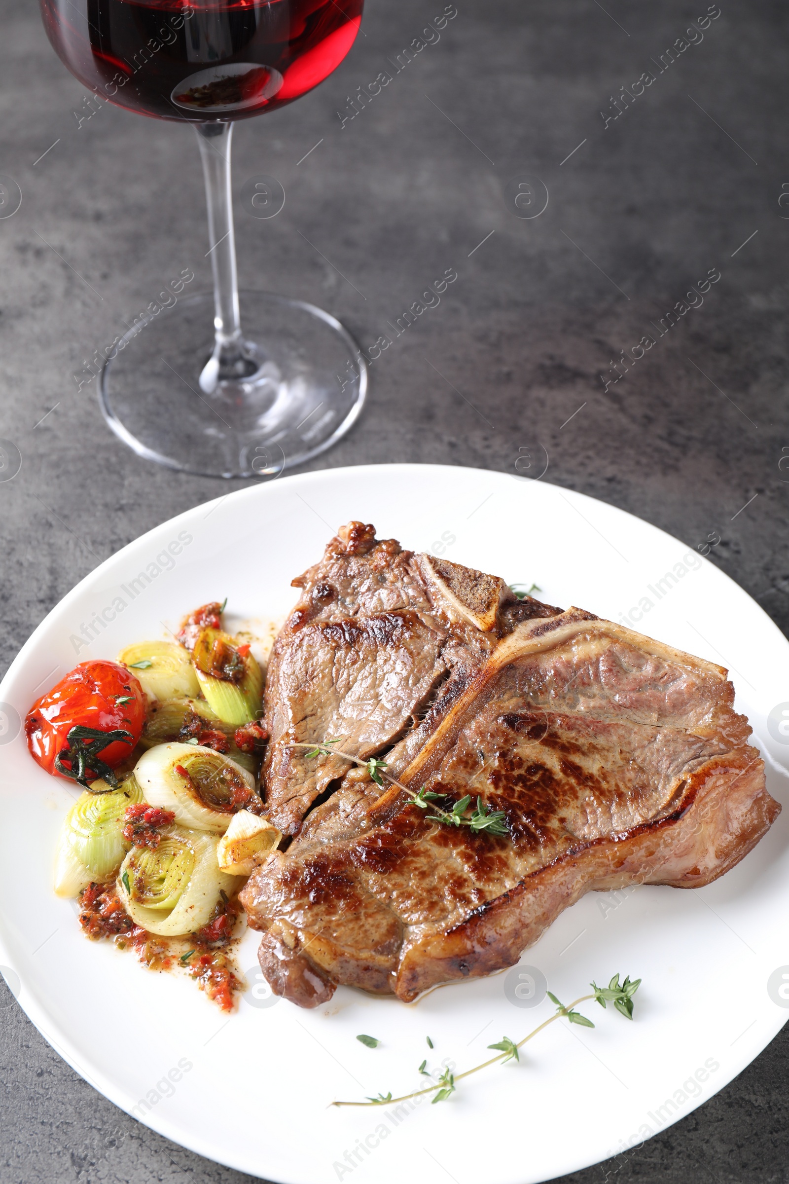 Photo of Delicious fried beef meat, vegetables and glass of wine on grey table