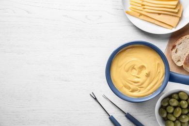 Flat lay composition with cheese fondue and products on white wooden table, space for text