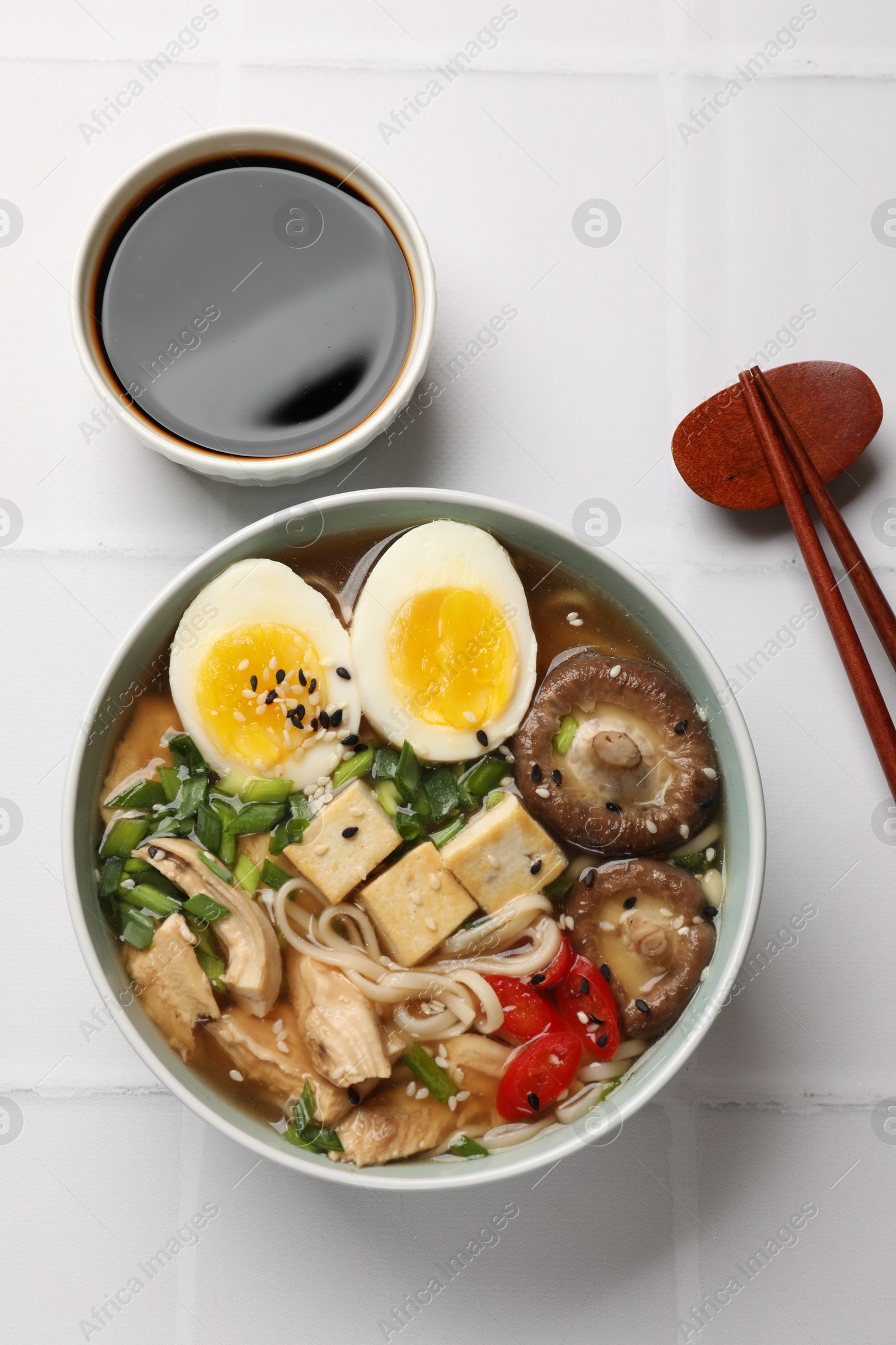 Photo of Noodle soup. Bowl of delicious ramen and chopsticks on white tiled table, top view