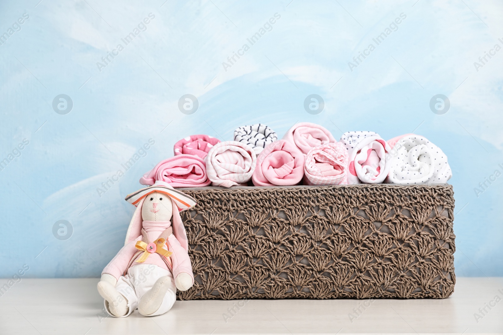 Photo of Basket with baby clothes and toy on table near color wall
