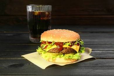 Photo of Burger with delicious patty and soda drink on black wooden table