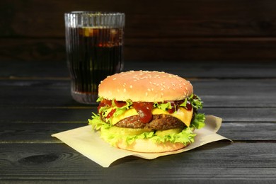 Burger with delicious patty and soda drink on black wooden table